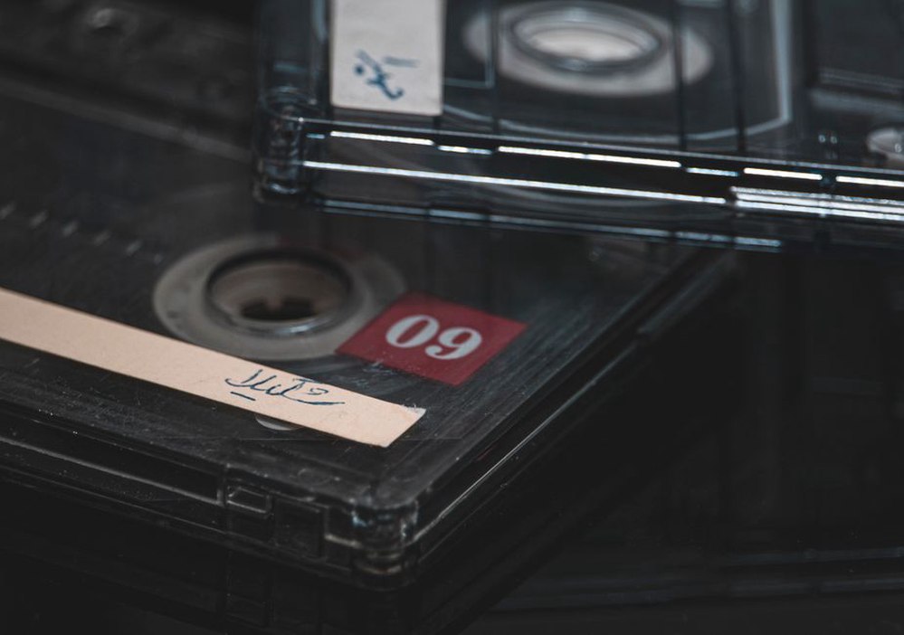 Hand-numbered cassette with exposed reels sits on a worn wooden desk