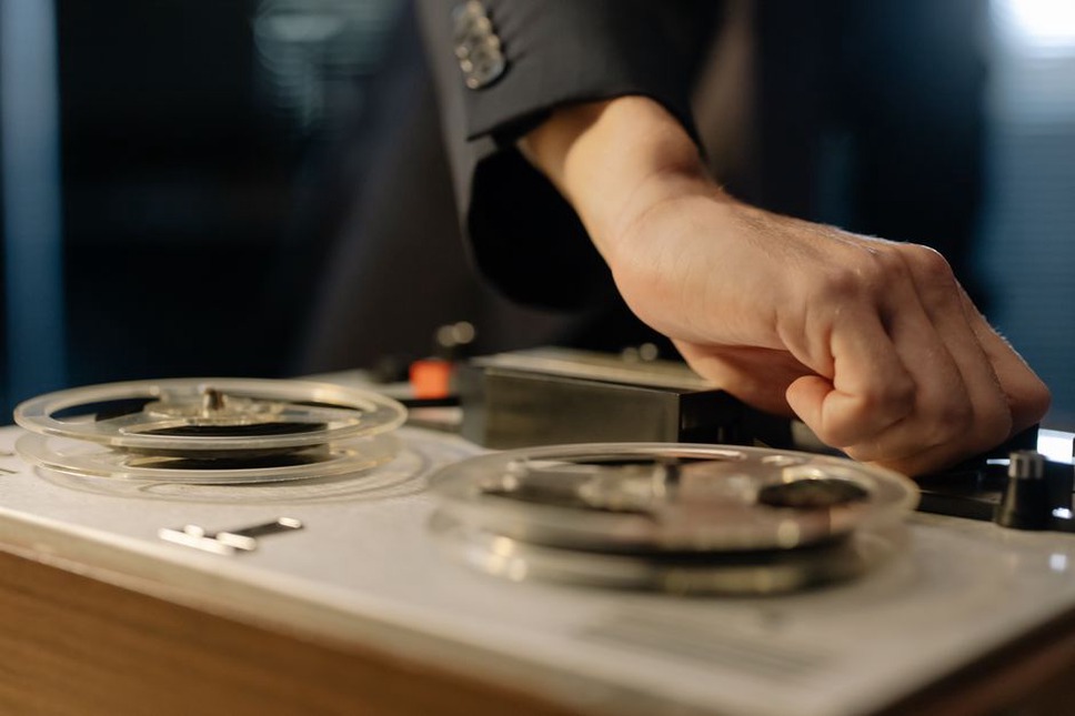 hands threading tape on a reel-to-reel recorder in low light