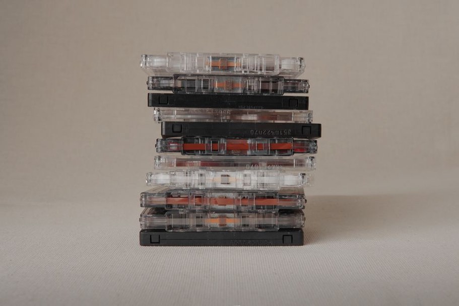 Several unlabeled cassettes stacked on a desk, each with a small handwritten code