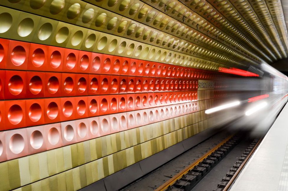 a train rushes through a narrow subway tunnel under harsh fluorescent light